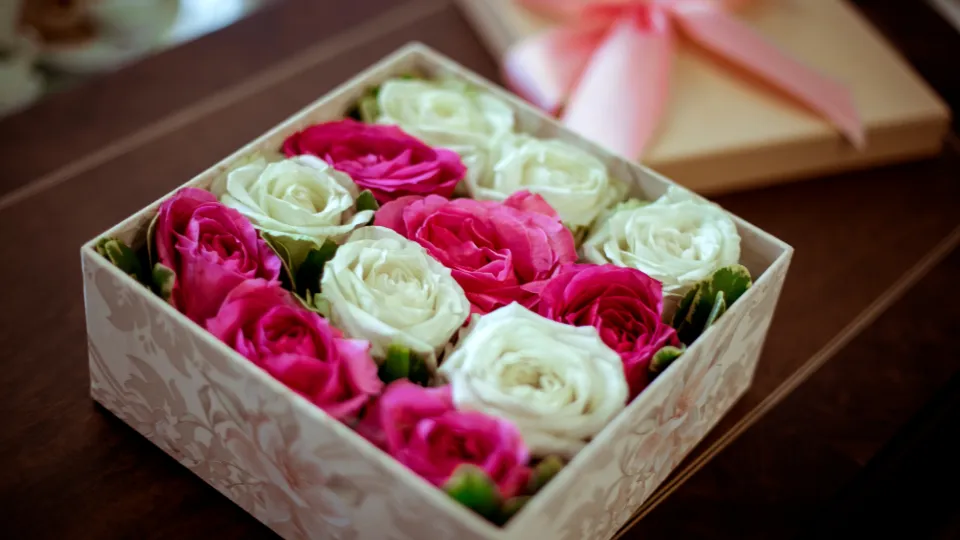 Geschenkbox mit rosa und weißen Rosen auf einem Holztisch